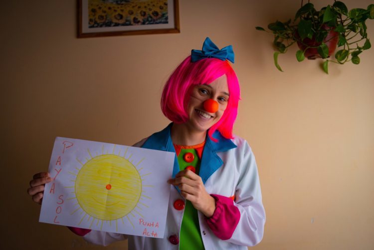 A woman dressed as a clown holds a large piece of paper