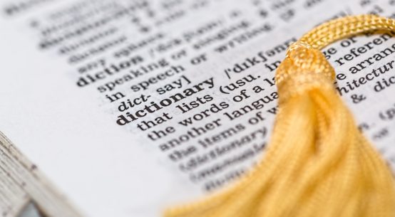 A dictionary is open to the word dictionary, with a yellow tassel bookmark laying across the page